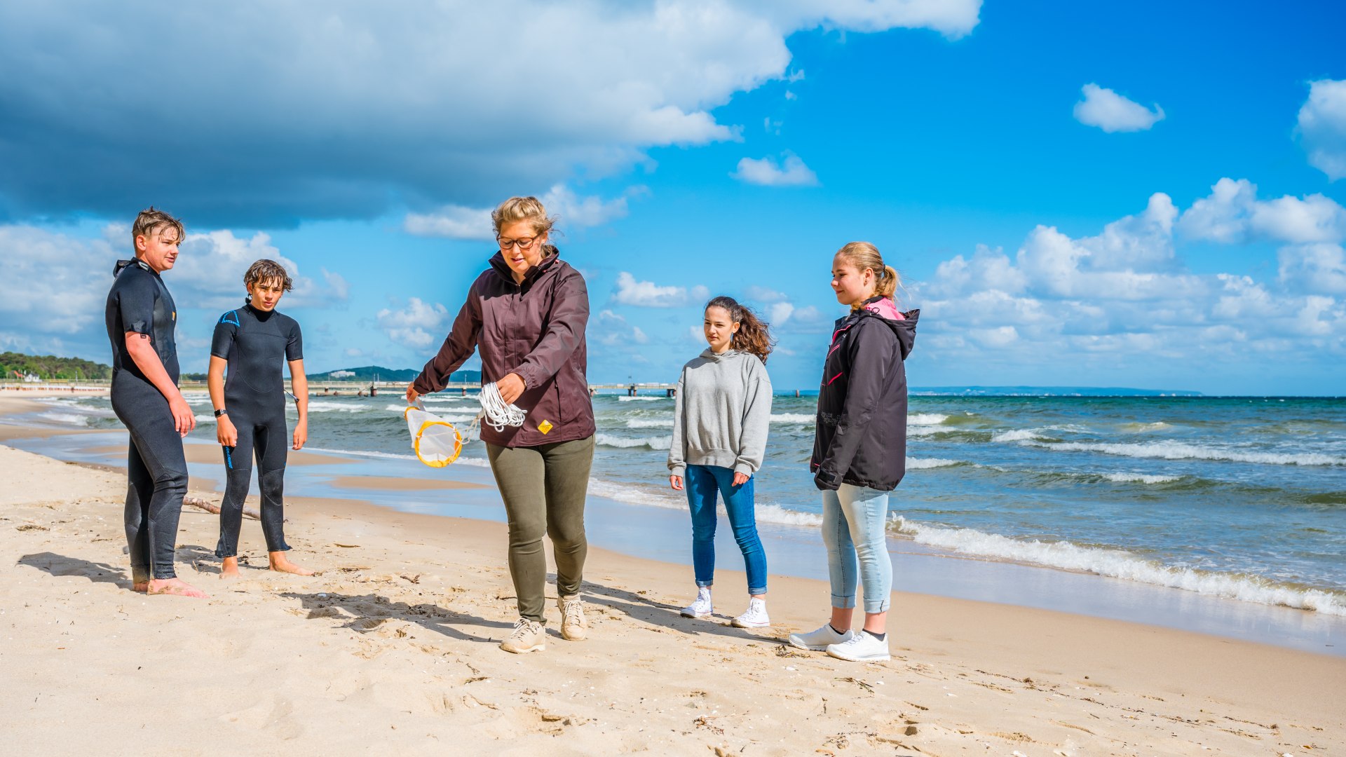 Eine Meeresbiologin zeigt ein kleines Schleppnetz zum Einfangen von Proben aus der Ostsee. Die Kinder um sie schauen gespannt zu.